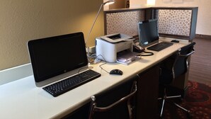 Un espace de travail dans un hôtel équipé d’un ordinateur portable, d’un ordinateur de bureau, d’une imprimante et de chaises de bureau.