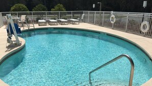 A clear swimming pool with a metal ladder, lounge chairs, and a fenced area with lifebuoys. - Holiday Inn Express Defuniak Springs by IHG (De Funiak Springs)