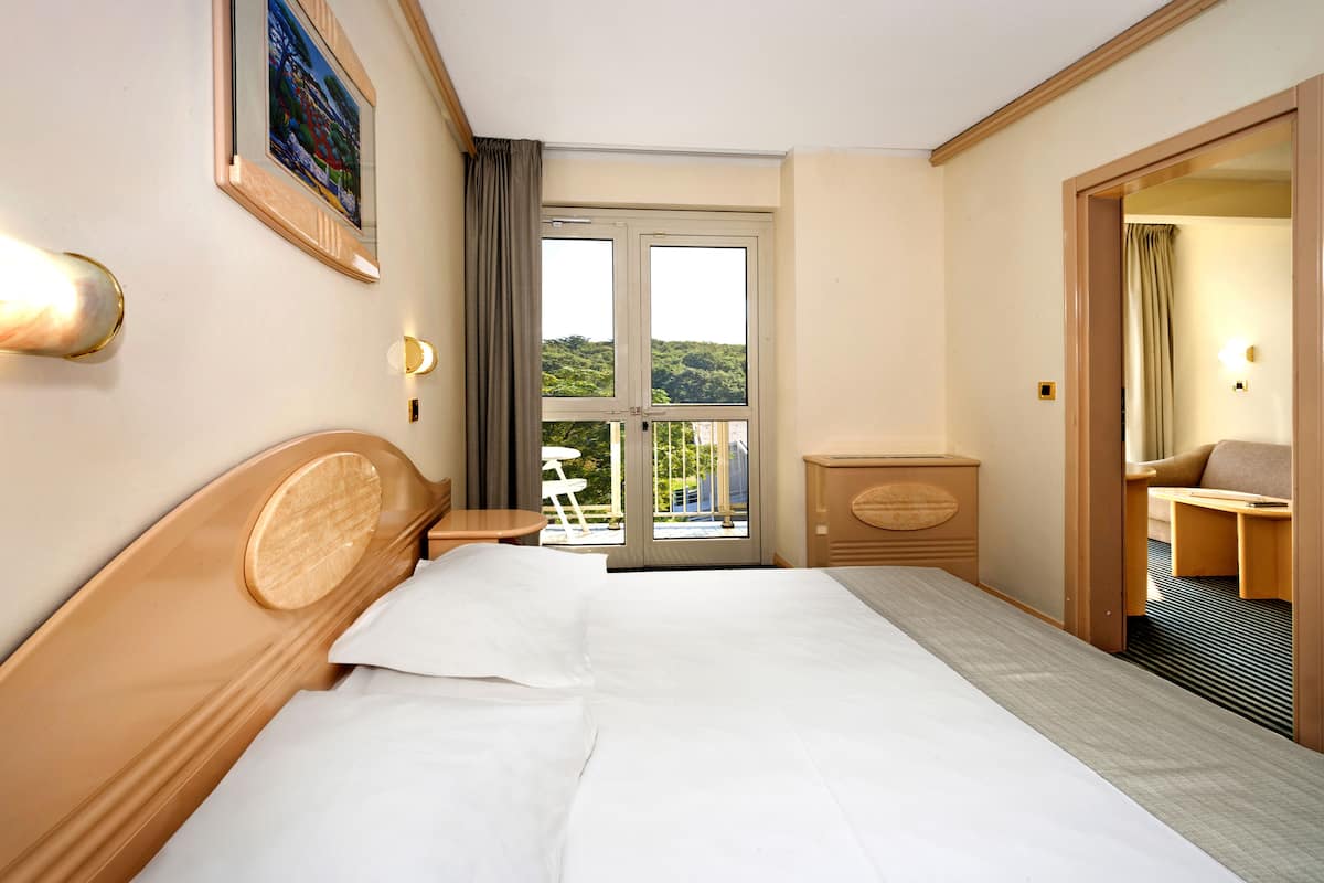A hotel room with a large bed, a small table, a chair, a desk, and a view of the outdoors.