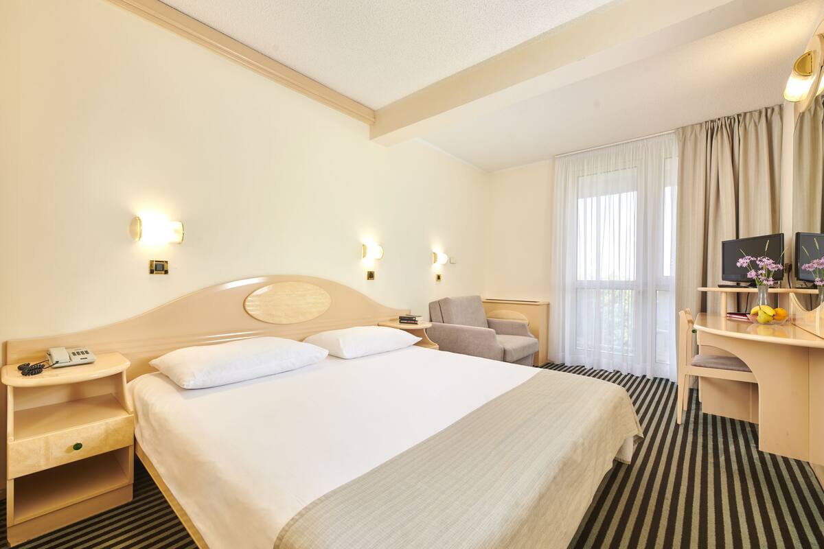 A hotel room with a large bed, bedside tables, a desk, and a chair.