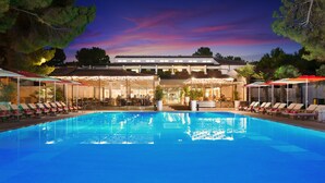 Ein Pool mit Liegestühlen und Sonnenschirmen, ein Restaurant mit Außenterrasse und ein Gebäude mit einer Dachterrasse.