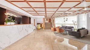 Eine großzügige Lobby mit einem Marmor-Empfangstresen, modernen Möbeln und einer Treppe zu den oberen Etagen.