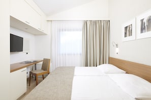 A hotel room with a bed, a desk with a chair, a television, and a window with curtains.