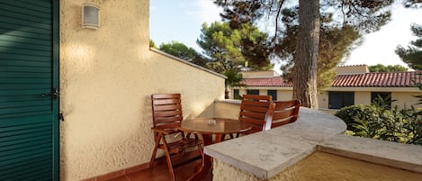 Une terrasse avec une table ronde et des chaises en bois, une porte verte et une vue sur les bâtiments et les arbres voisins.