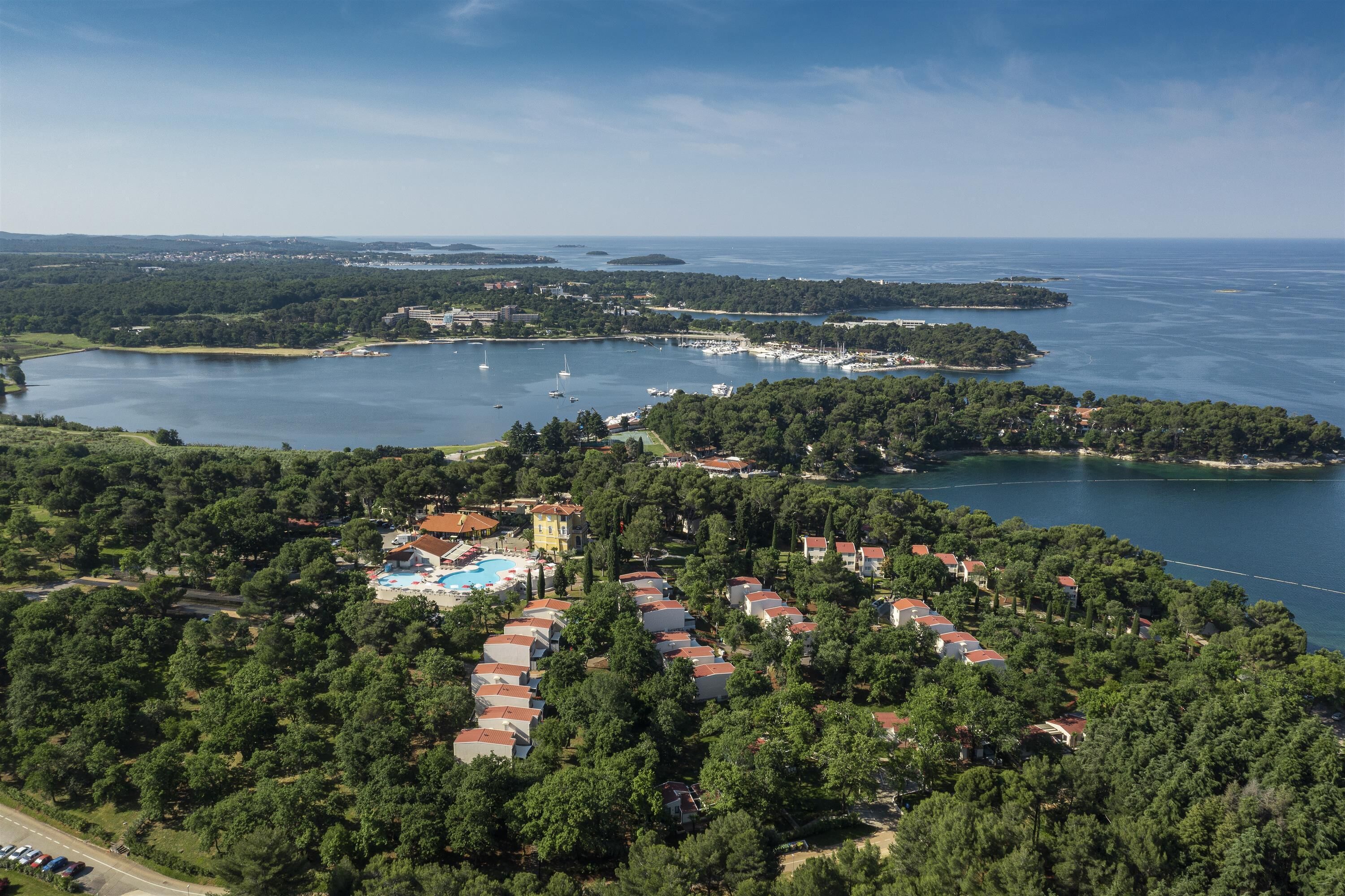 An aerial view of a coastal resort with multiple villas, a marina, and a large body of water.
