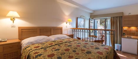A hotel room with a bed, bedside tables, a desk, a chair, a balcony, and a kitchenette.