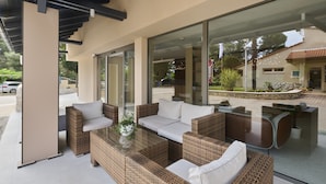 Un espace extérieur moderne, aménagé avec des meubles en osier et une table en verre, offrant une vue sur un jardin paysager et une rue.