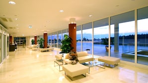Eine großzügige Lobby mit einer Rezeption, Sitzbereichen und großen Fenstern mit Blick ins Freie.