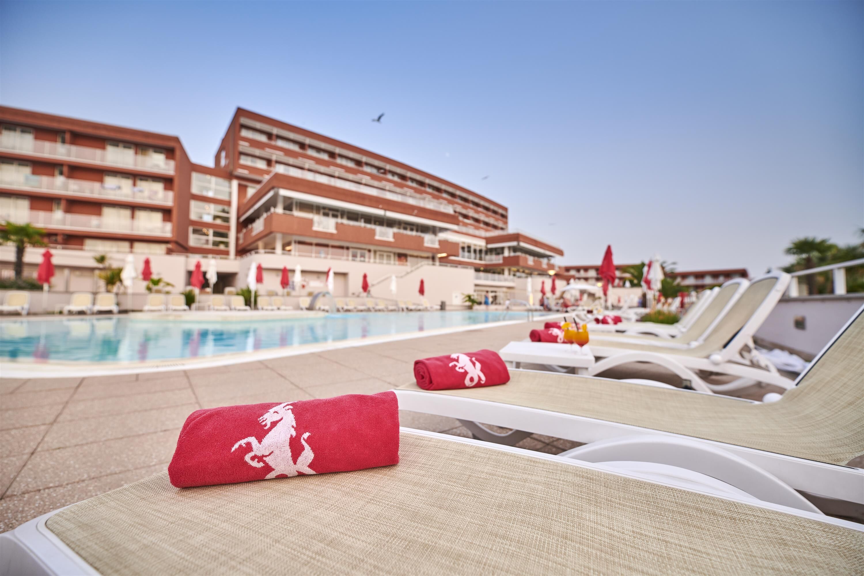 A poolside area with lounge chairs, a swimming pool, and a hotel building in the background.