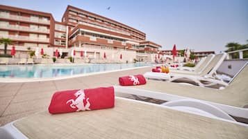 A poolside area with lounge chairs, a swimming pool, and a hotel building in the background.
