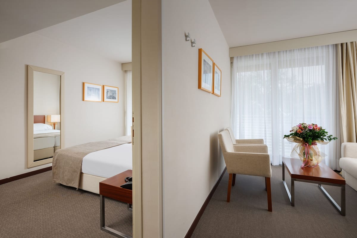 A hotel room with a bed, bedside table, chair, and a small table with a vase of flowers.