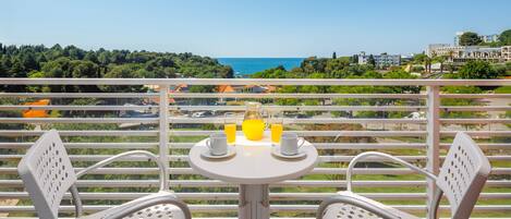 Un balcón con una mesa y dos sillas, con vista a un paisaje marítimo y exuberante.