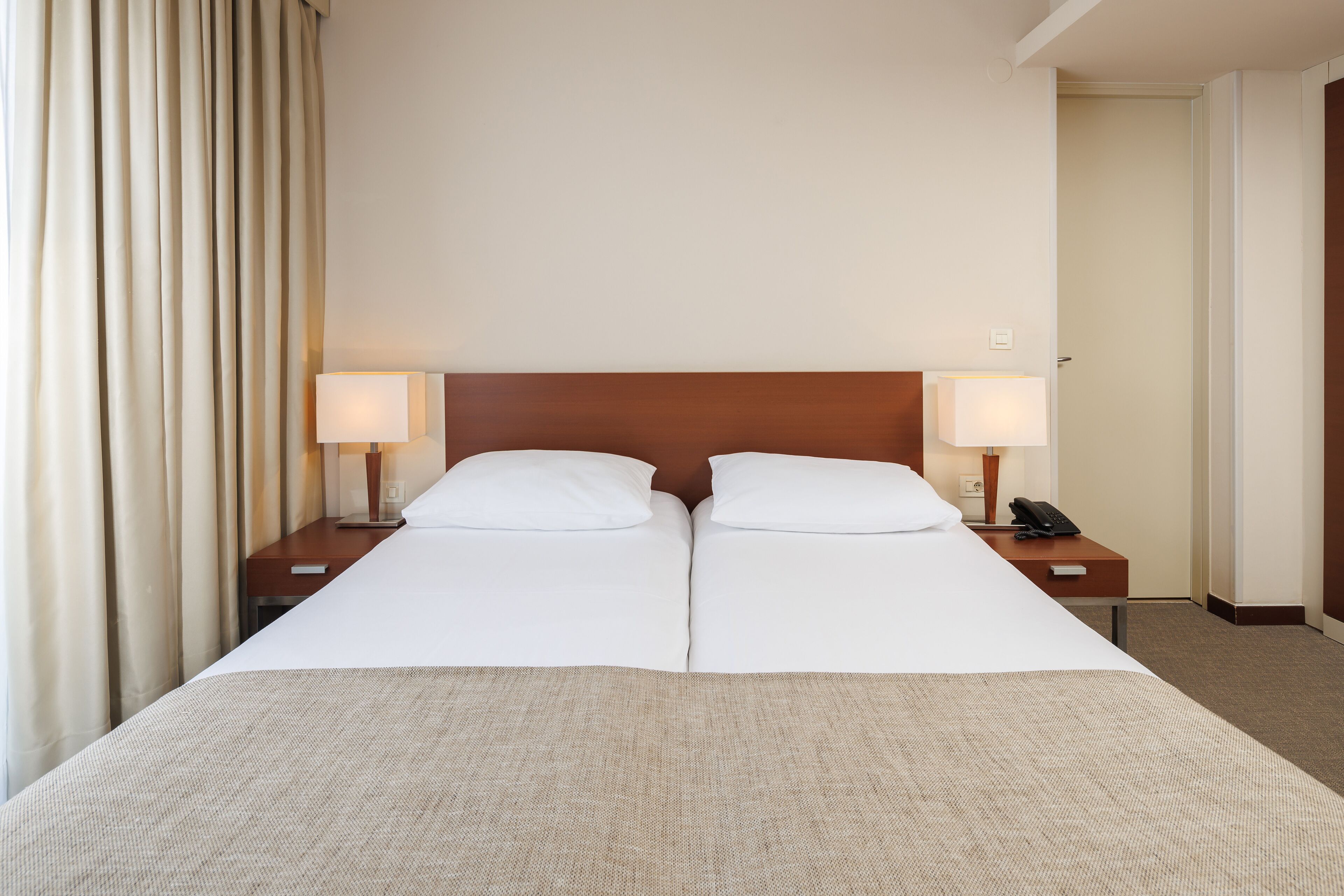 Una cama doble con ropa de cama blanca, dos mesitas de noche con lámparas y un cabecero de madera.