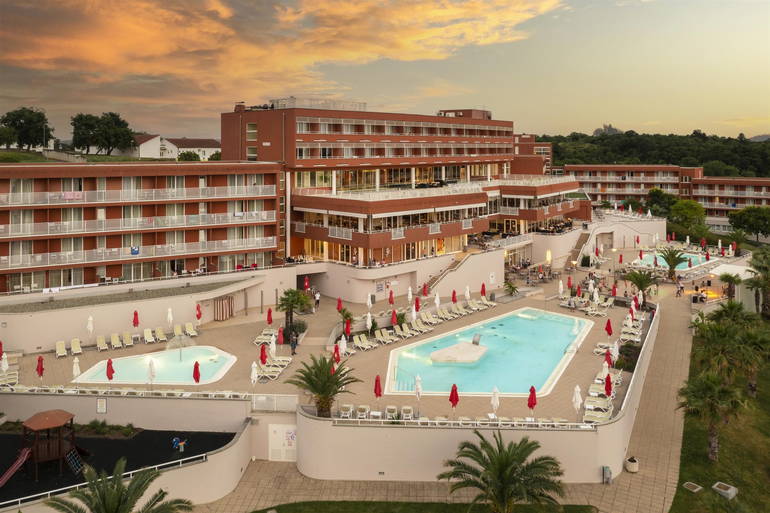 Un hotel con varios pisos, piscinas al aire libre y tumbonas.