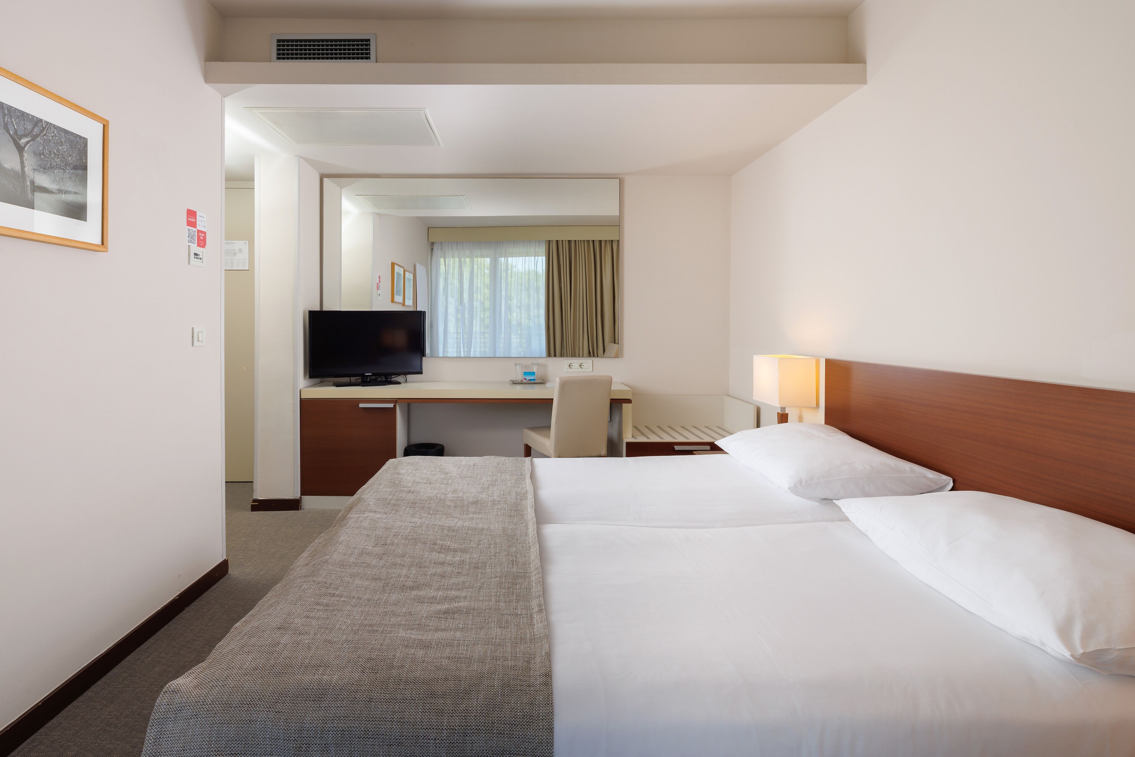 Una habitación de hotel con cama, escritorio, televisor y espejo.