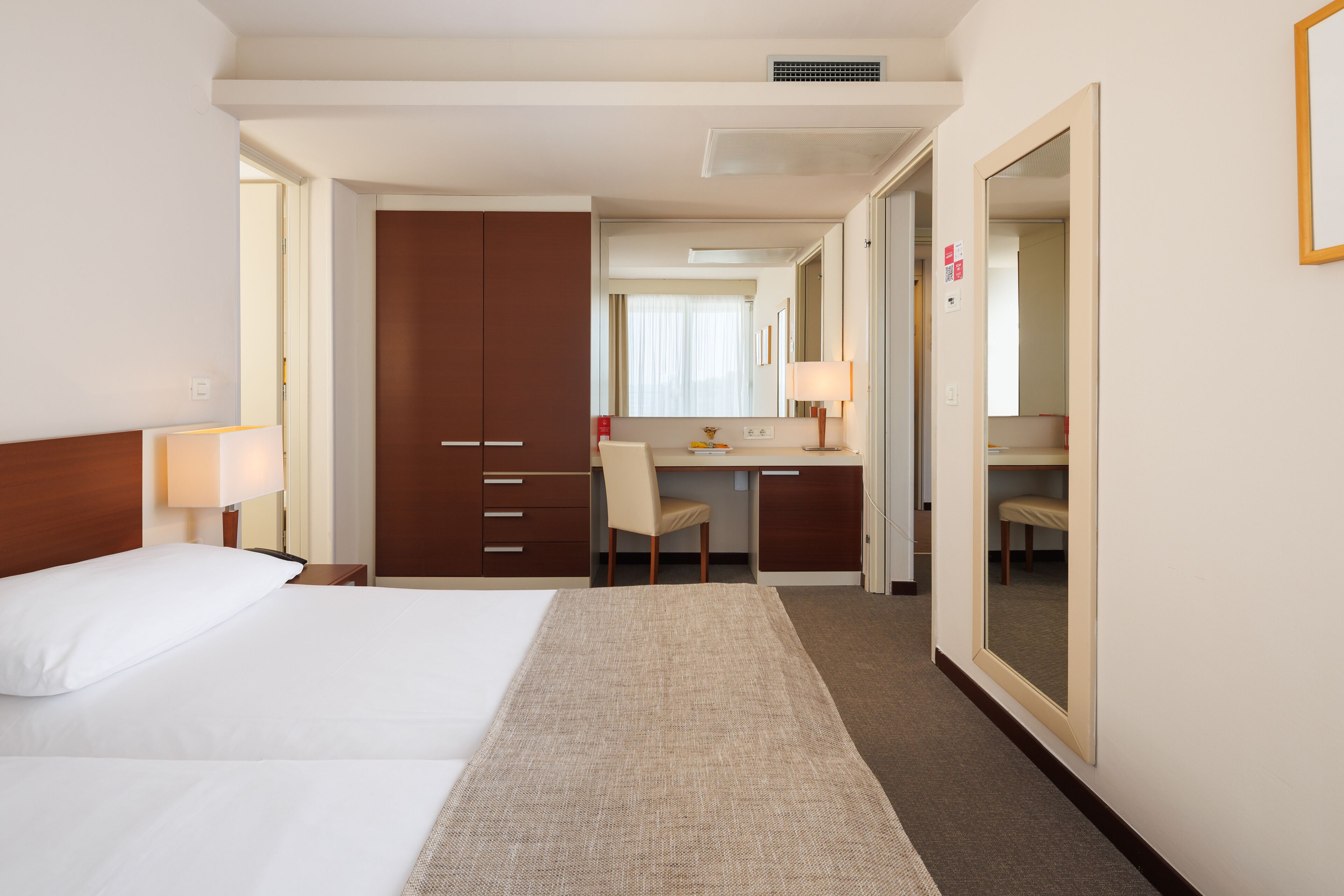 Une chambre d’hôtel comprenant un lit, un bureau, une chaise, un miroir et une armoire.