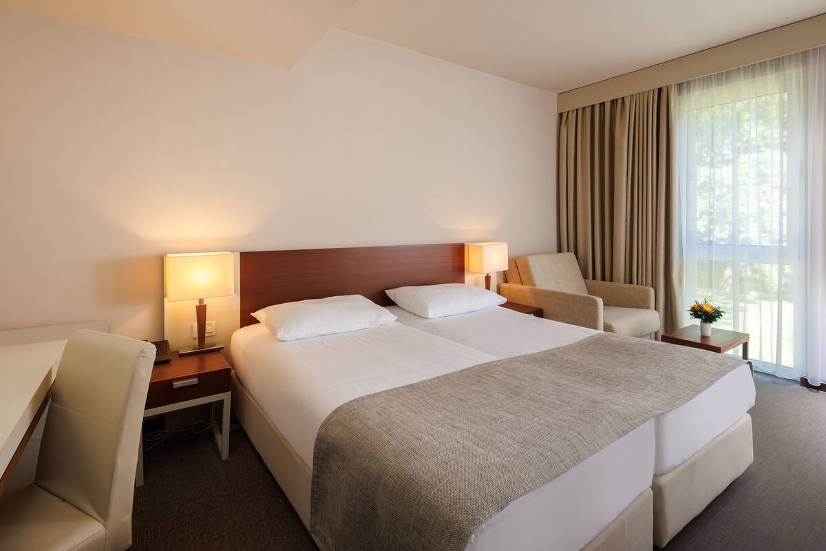 A hotel room with a large bed, two bedside tables, a chair, and a window with curtains.