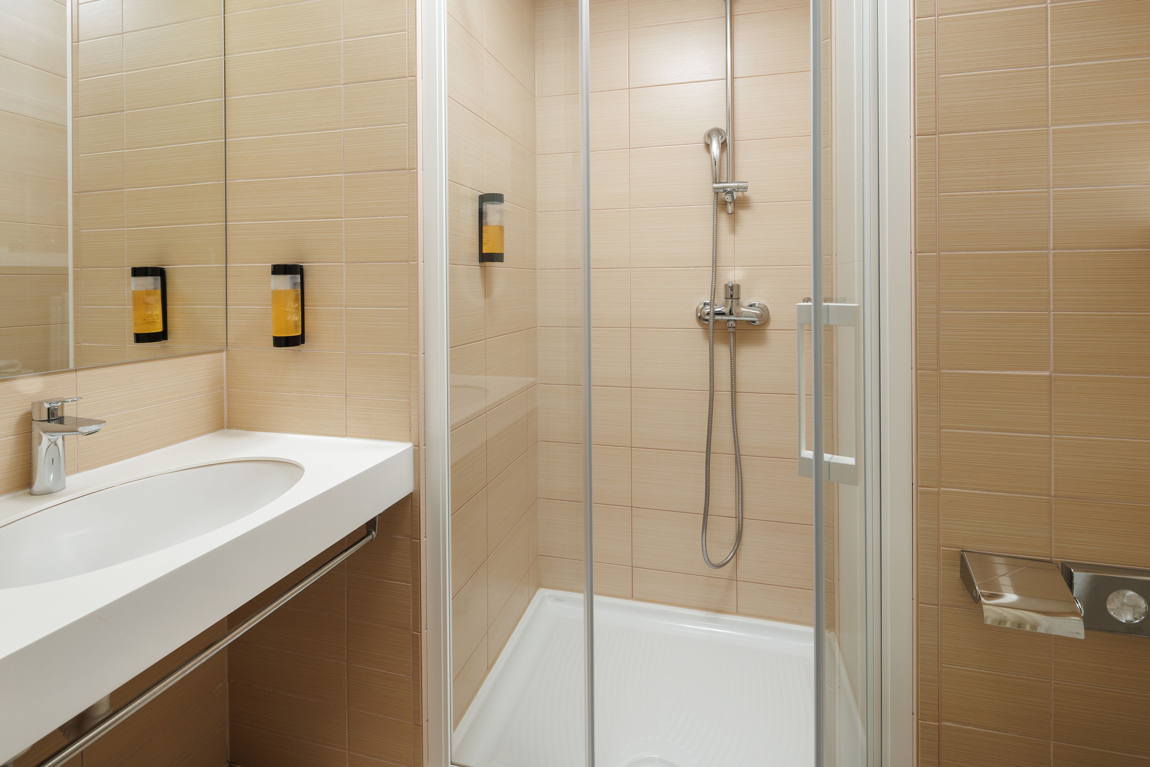 Un baño moderno con ducha envuelta en vidrio, un lavabo blanco y baldosas color beige.