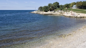 Ein Kiesstrand mit klarem Wasser, einem Pavillon und einer Parkanlage mit Personen.