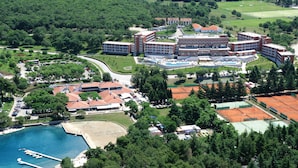 Ein Luftbild eines Hotels mit mehreren Gebäuden, einem Schwimmbad, Tennisplätzen und einer Strandbucht mit Booten.