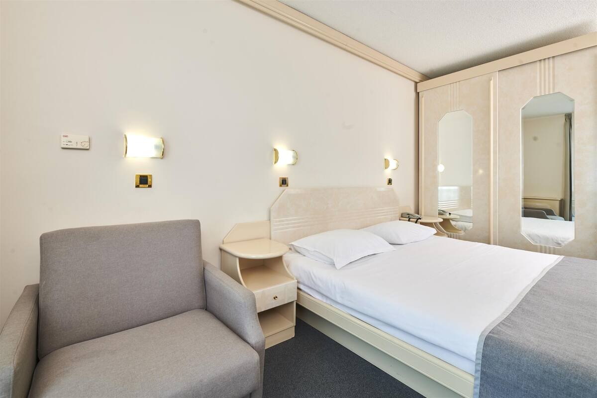 Een hotelkamer met een bed, een stoel, een nachtkastje en een spiegel.