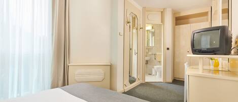 Una habitación de hotel con cama, televisión, baño y espejo.