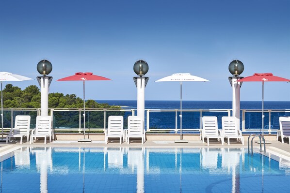 A poolside area with white lounge chairs and red umbrellas, overlooking a clear blue sky and ocean. - Hotel Gran Vista Plava Laguna (Porec)