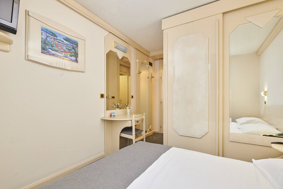 Een hotelkamer met een bed, nachtkastje, spiegel, douche en een schilderij aan de muur.