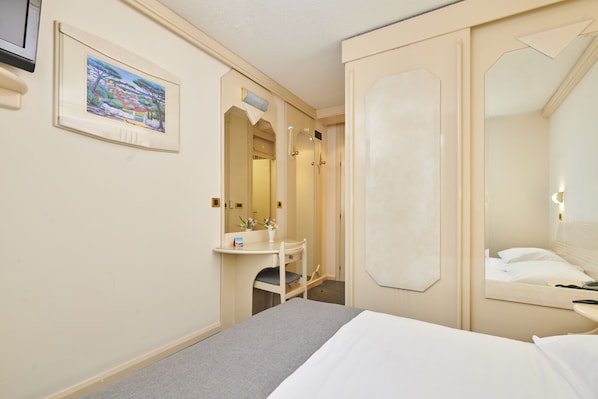 Quarto de hotel com cama, mesa de cabeceira, espelho, área de banho e um quadro na parede.