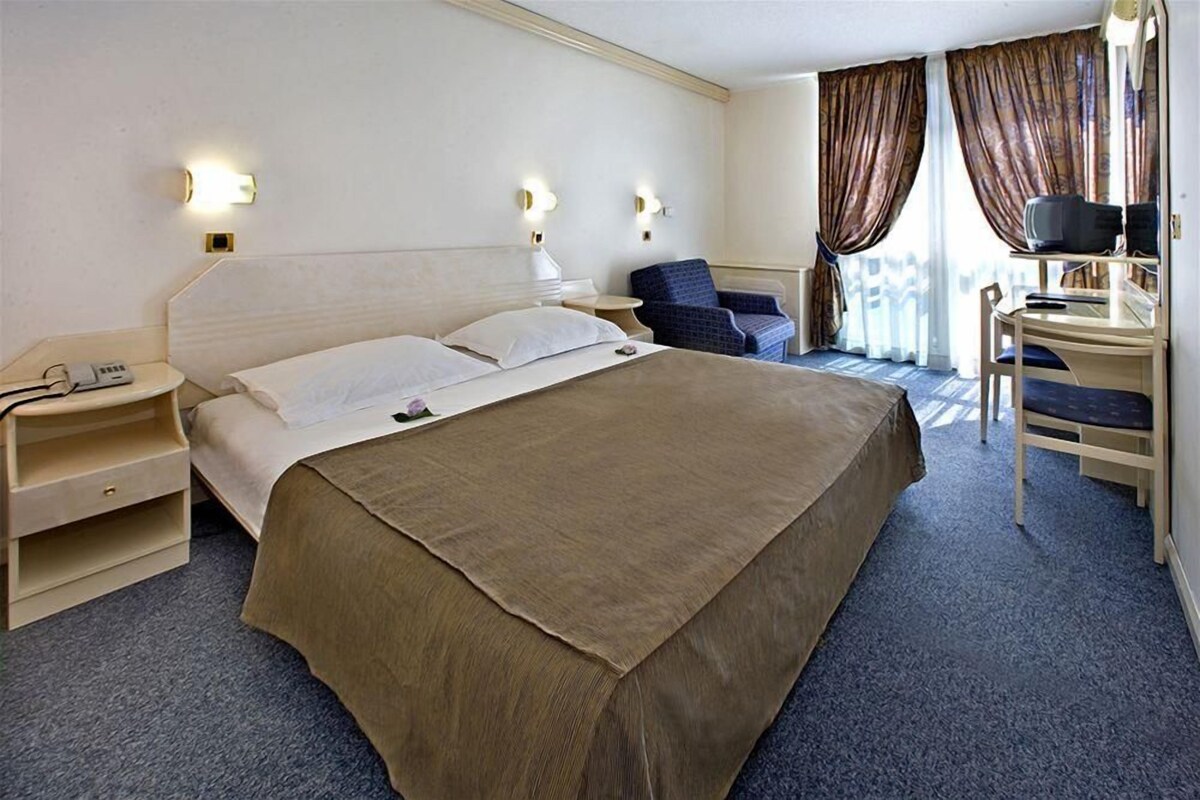 Een hotelkamer met een groot bed, nachtkastjes, een bureau met stoel en een televisie.