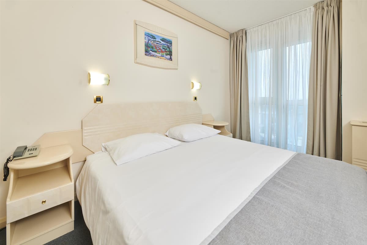 Een hotelkamer met een groot bed, nachtkastjes, een telefoon en een schilderij aan de muur.