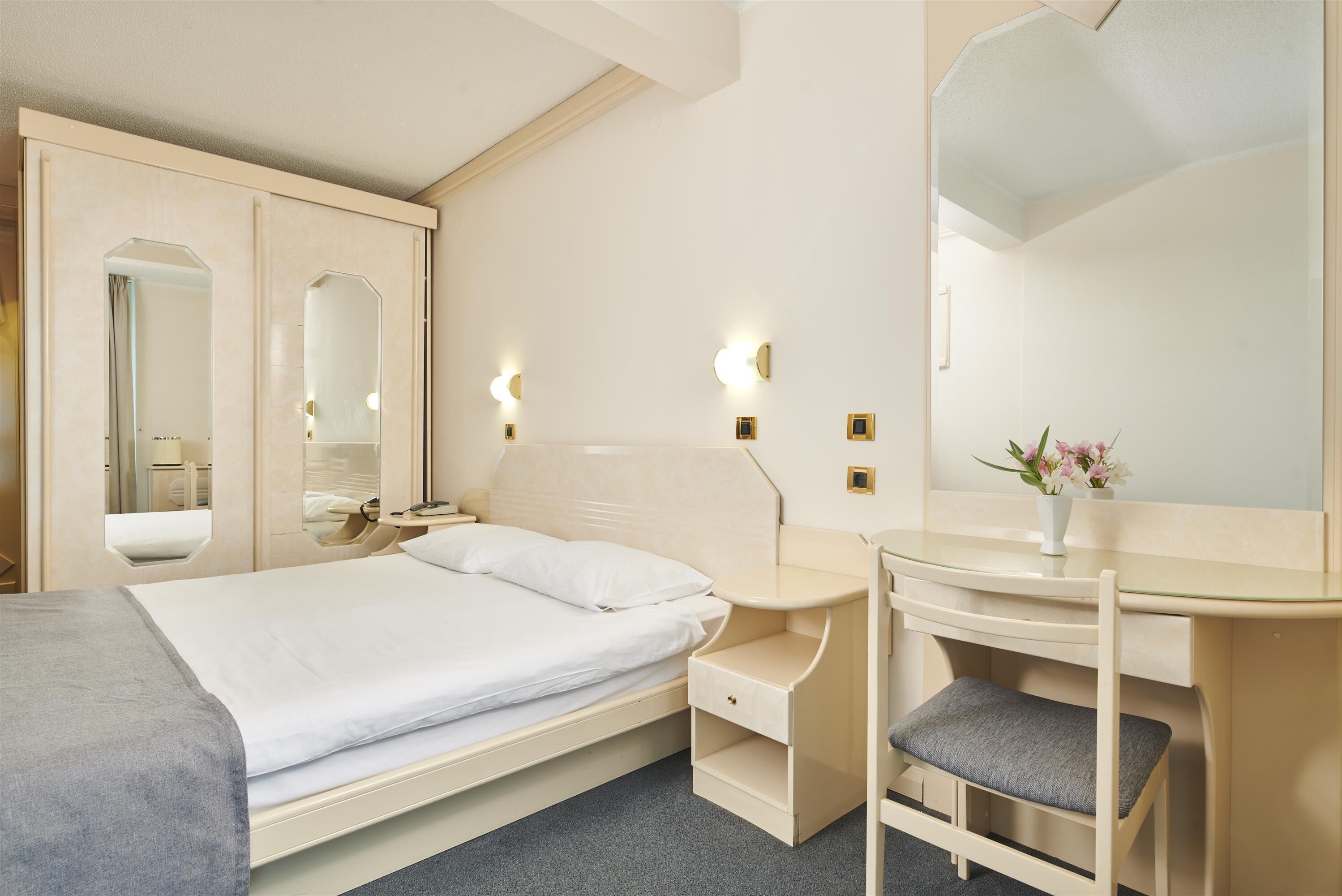 Habitación de hotel con cama, mesita de noche, silla y un espejo grande.