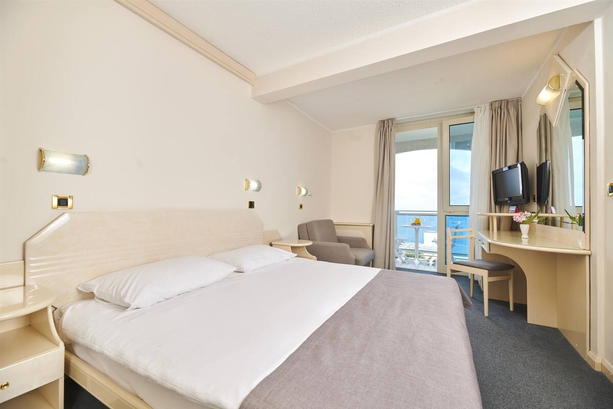 Hotelkamer met een bed, nachtkastje, stoel, bureau, televisie en balkon met uitzicht.