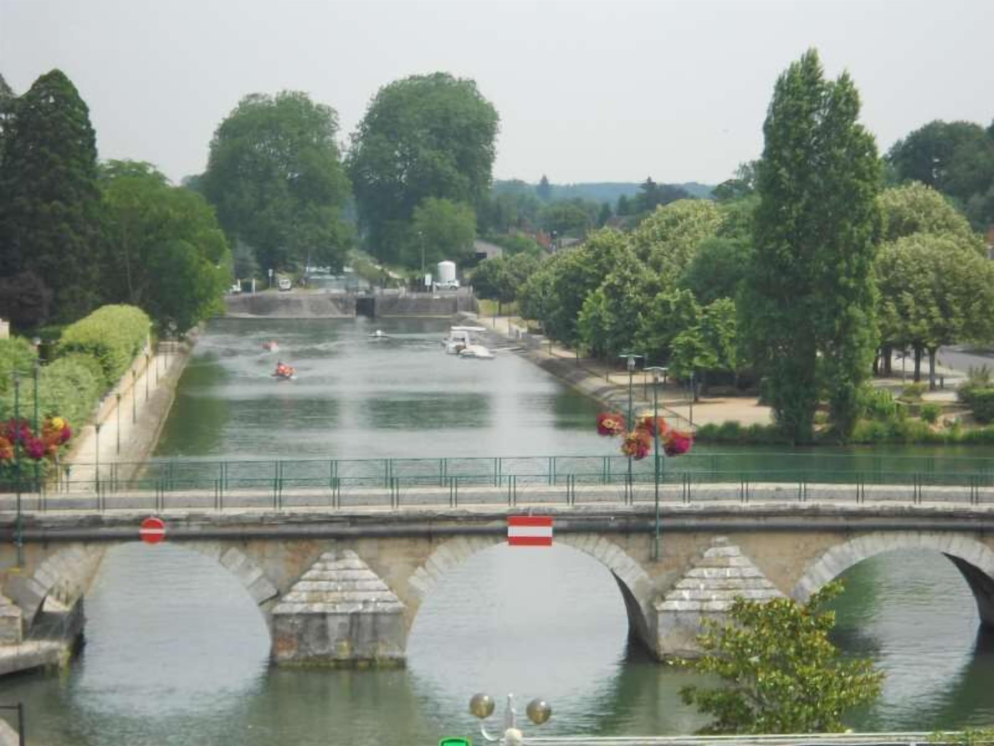 A stone bridge with three arches over a calm river, surrounded by lush greenery and trees.