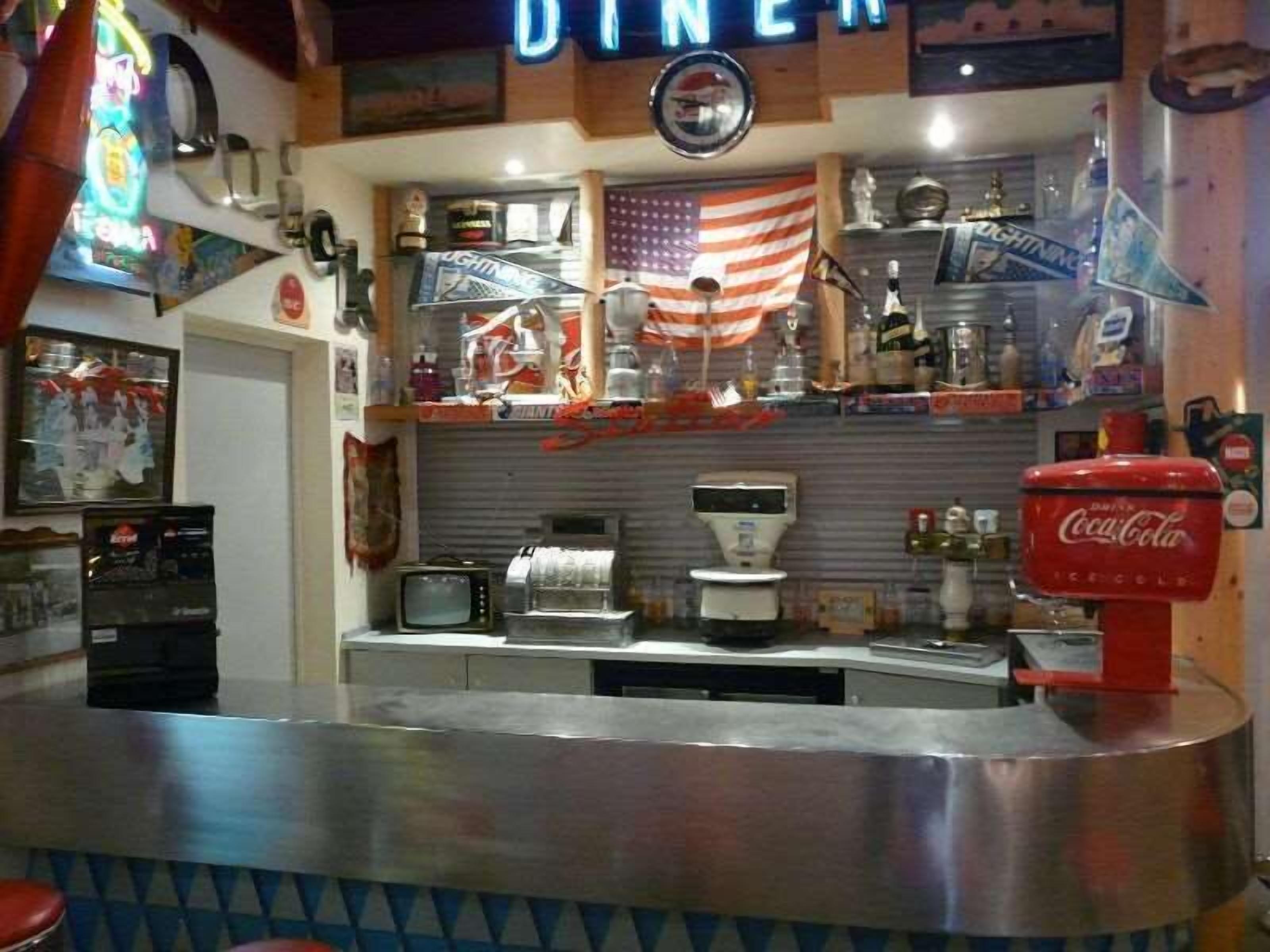 Un restaurante con decoración retro, que incluye un radiolas, un dispensador de Coca-Cola y una bandera estadounidense.