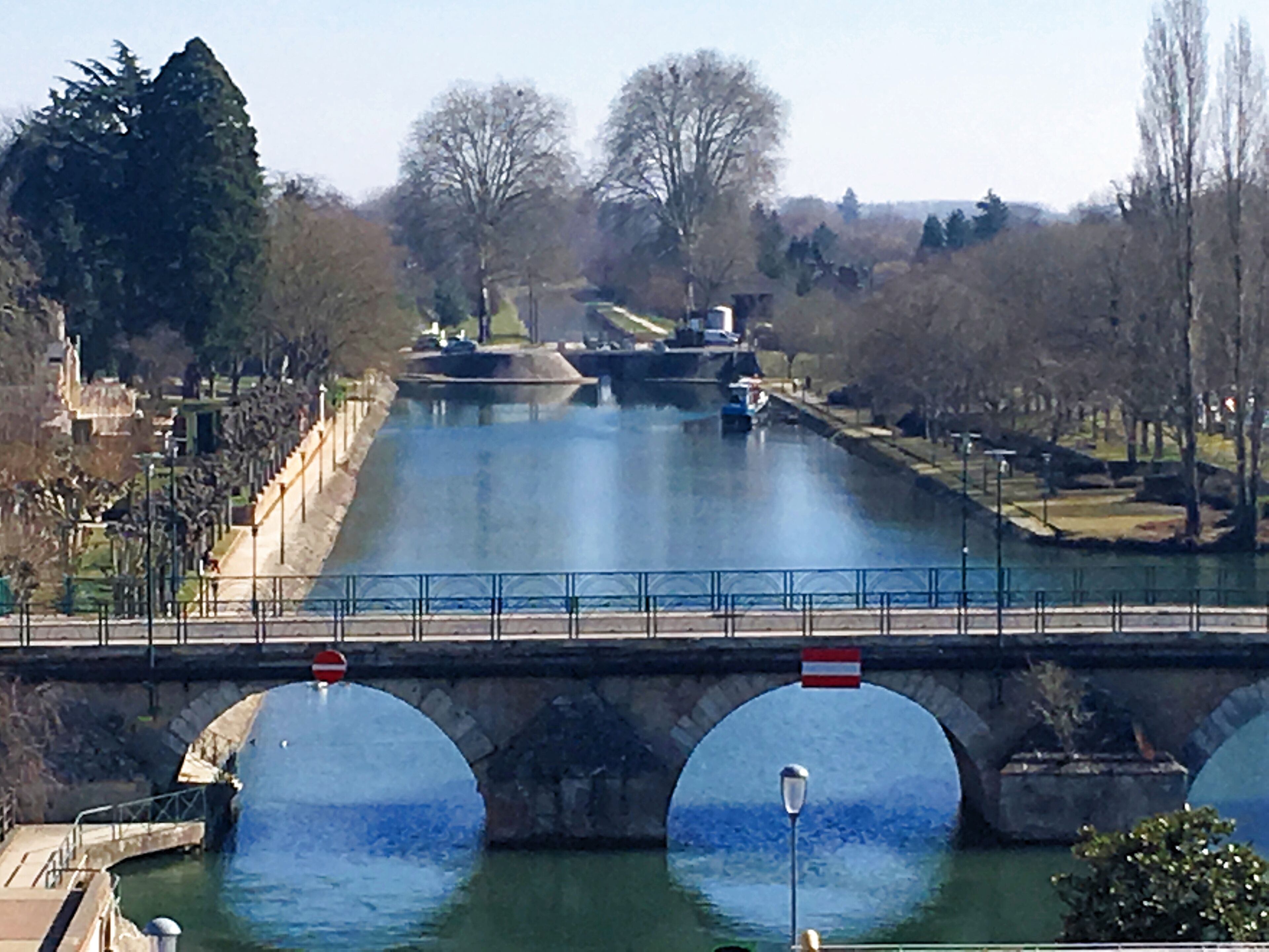 A river with a bridge, stone walls, and a row of trees.