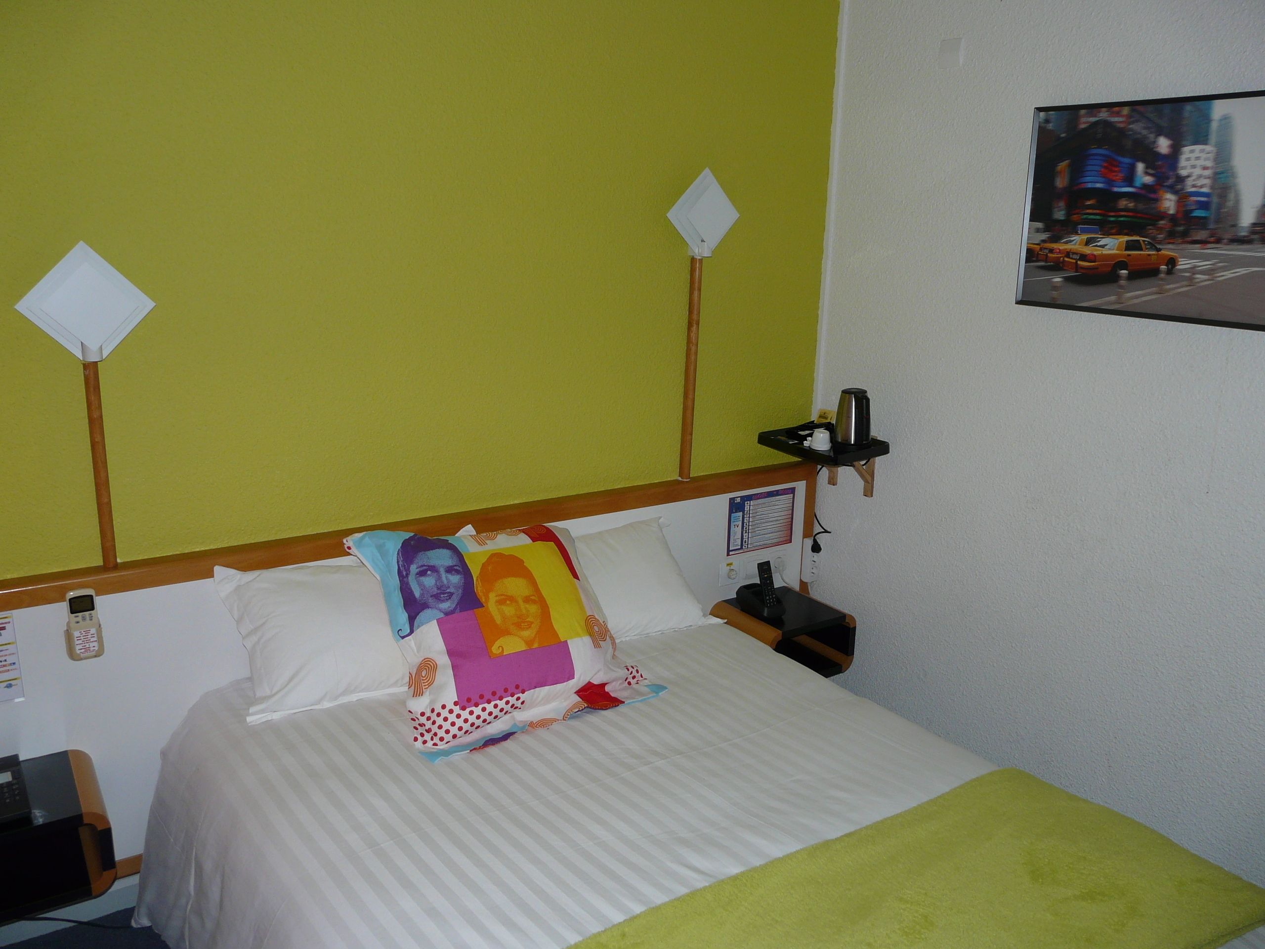 Een hotelkamer met een bed, een nachtkastje, een aan de muur bevestigde televisie en een groene wand.