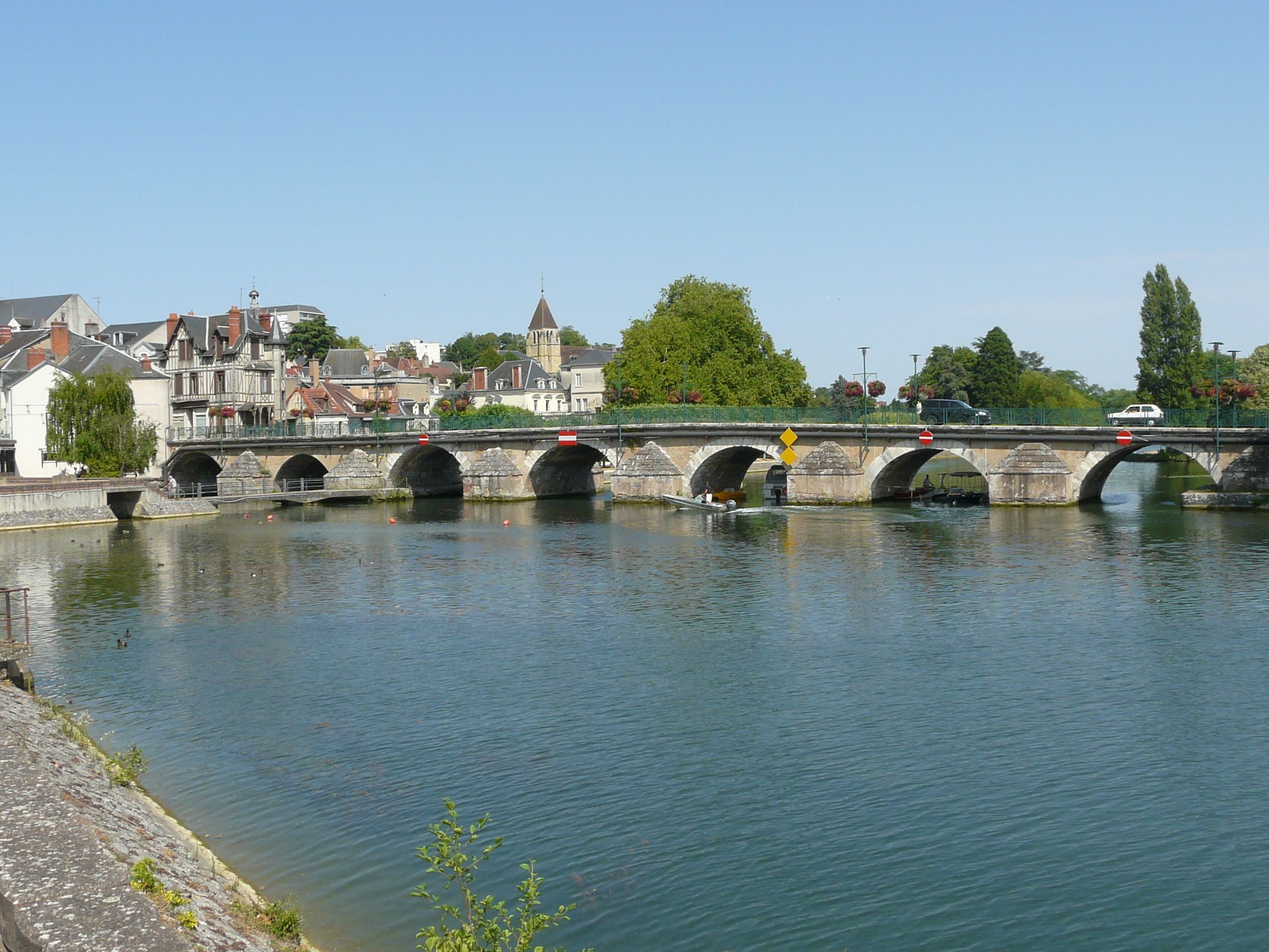 A stone bridge over a river with a town in the background.