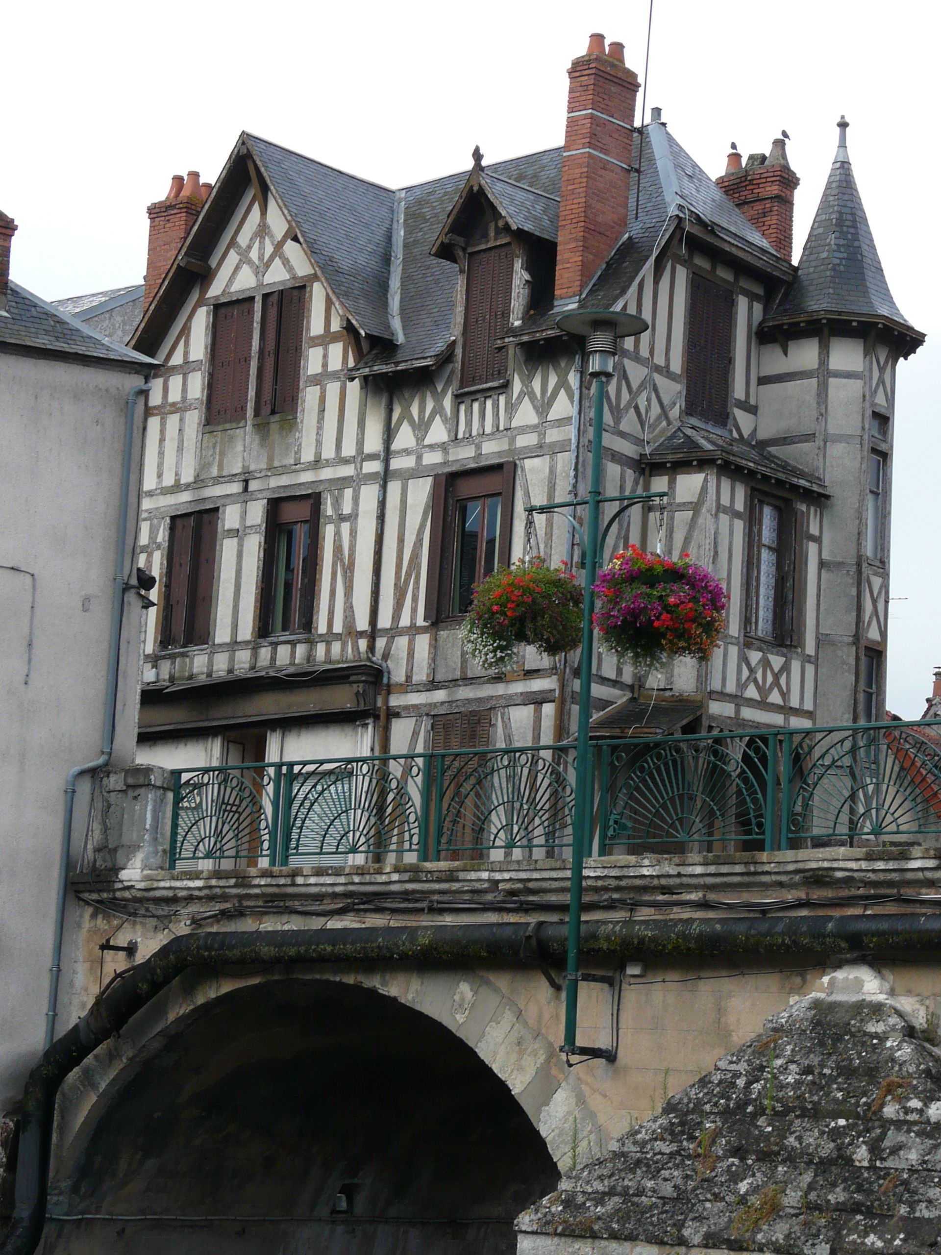 A half-timbered house with a balcony, a stone bridge, and a tunnel entrance.