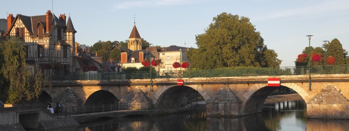 A stone bridge with arches over a river, surrounded by trees and buildings.