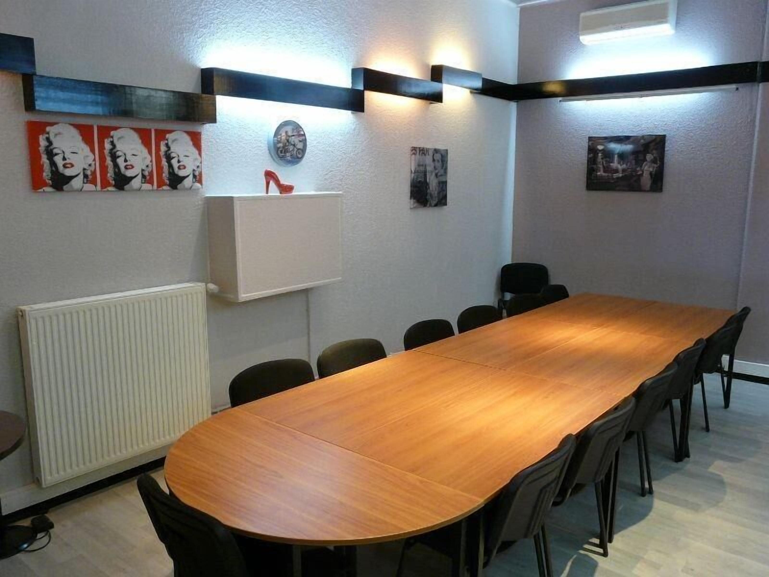 Un salón de conferencias con una larga mesa de madera, sillas negras y obras de arte colgadas en la pared.