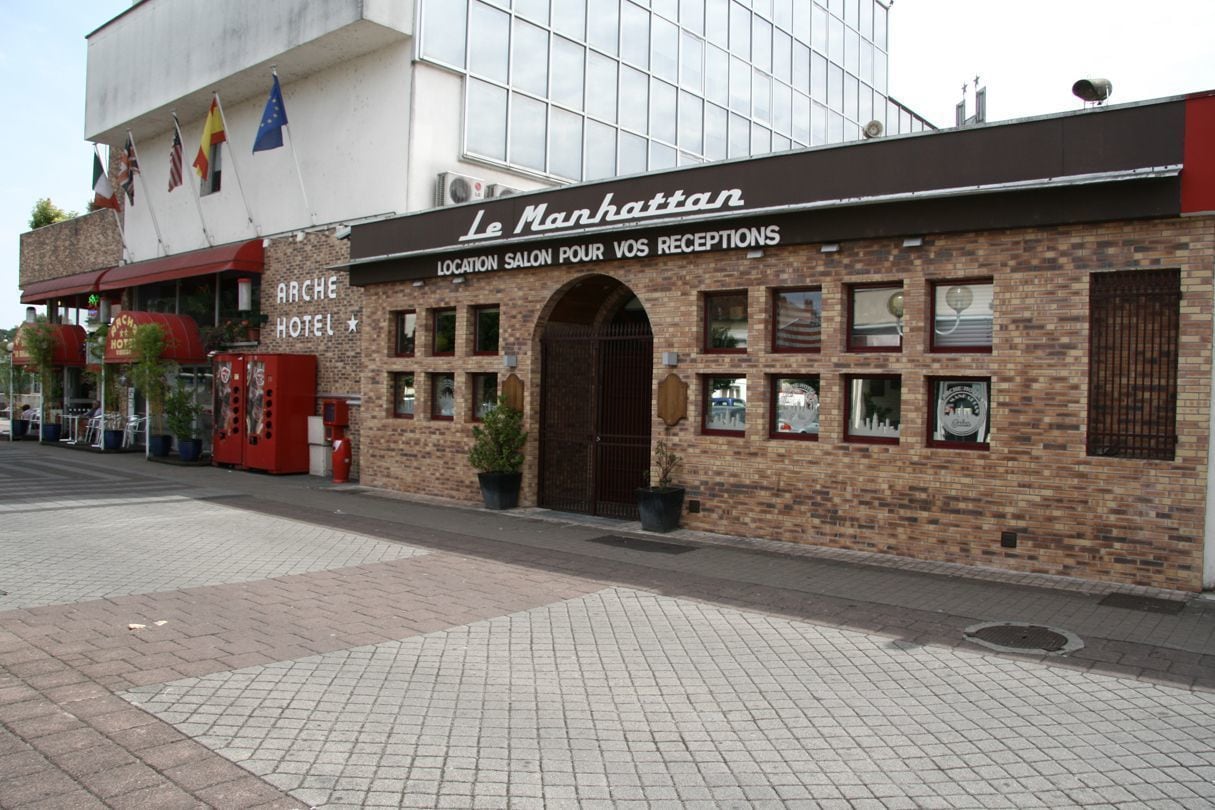 Een gebouw van baksteen met een bord waarop staat: "Le Manhattan" en "Location Salon pour vos Receptions".