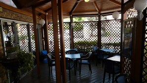 An outdoor patio area with tables and chairs, wooden beams, and lattice panels. - Arche Hotel (Vierzon)