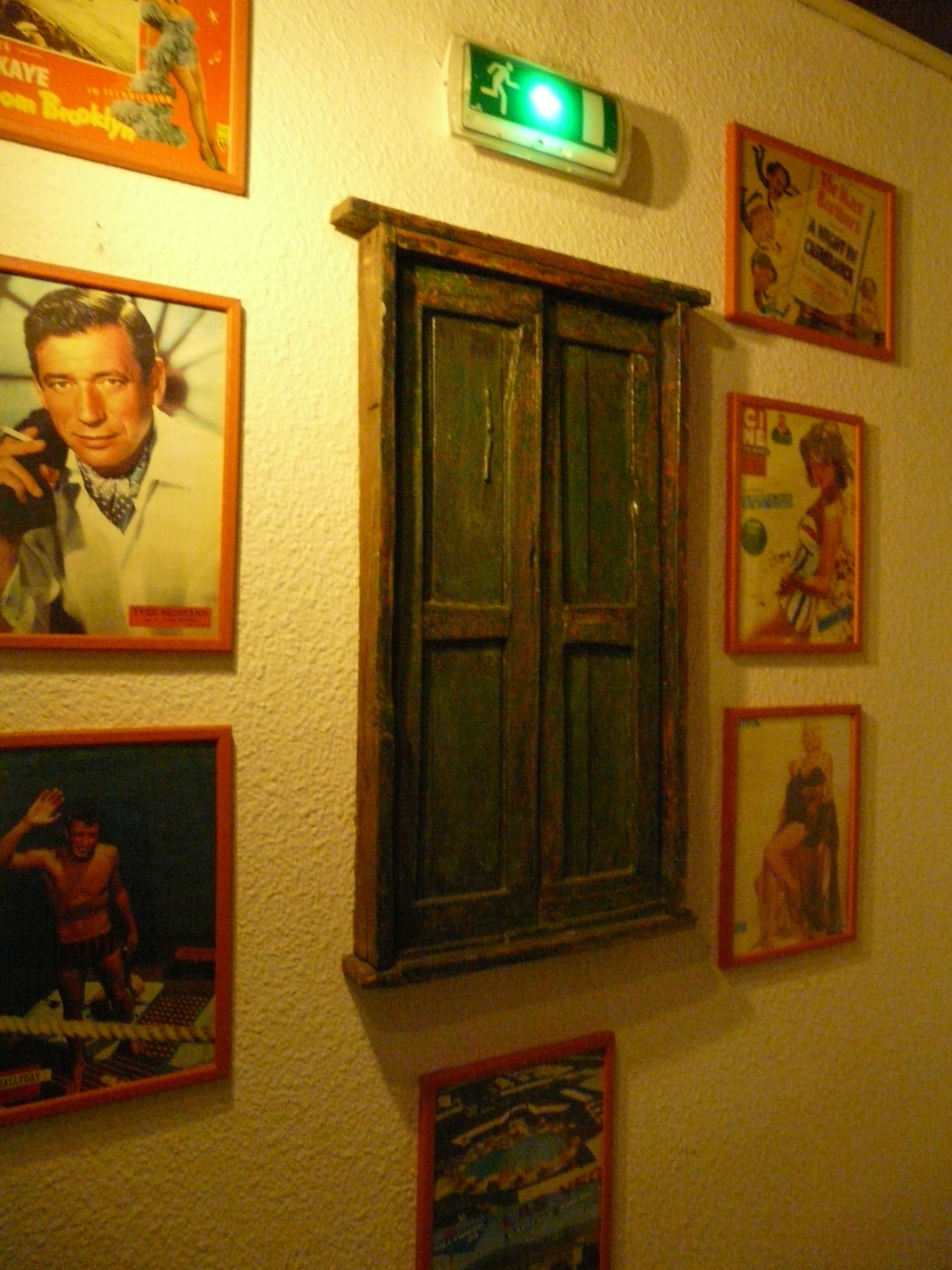 A wall with framed pictures, a green exit sign, and a wooden door.
