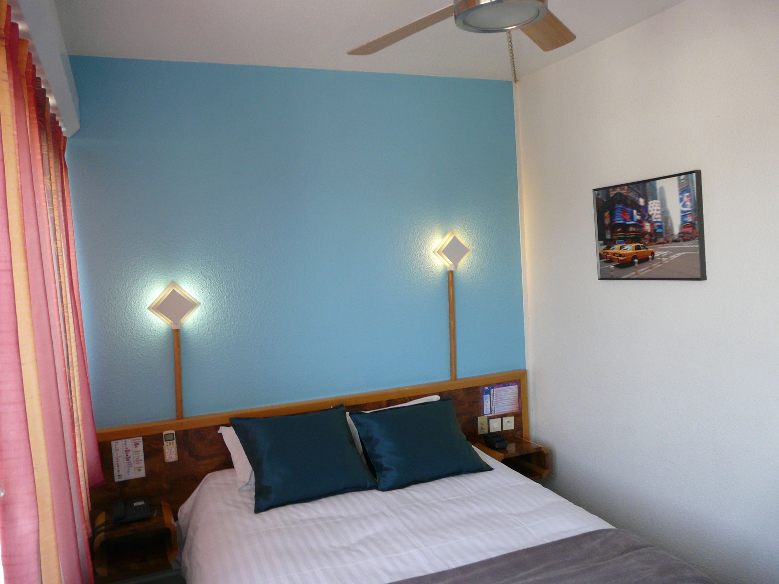 A hotel room with a bed, two bedside tables, a ceiling fan, and a wall-mounted picture.