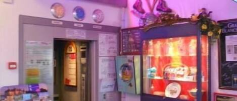 A brightly lit arcade area with neon signs, a vending machine, and a display of magazines.