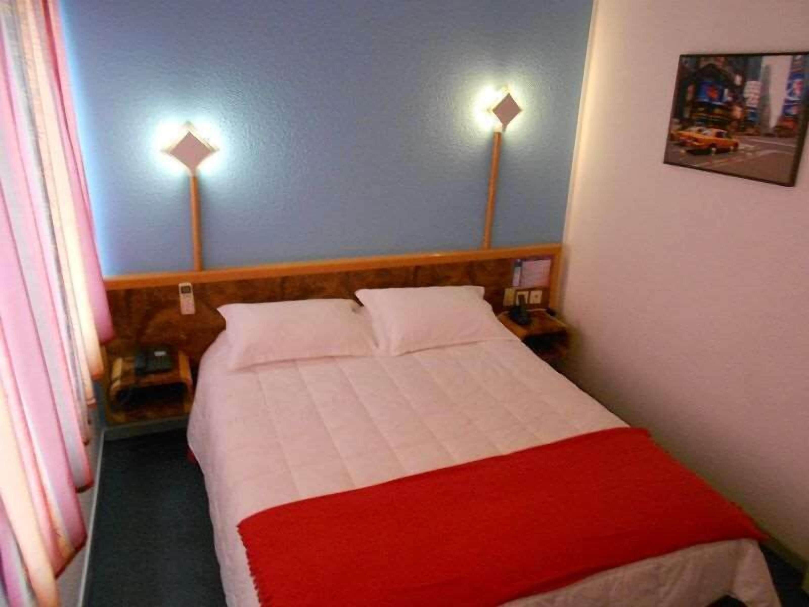A hotel room with a bed, two bedside lamps, a nightstand, and a wall-mounted picture.