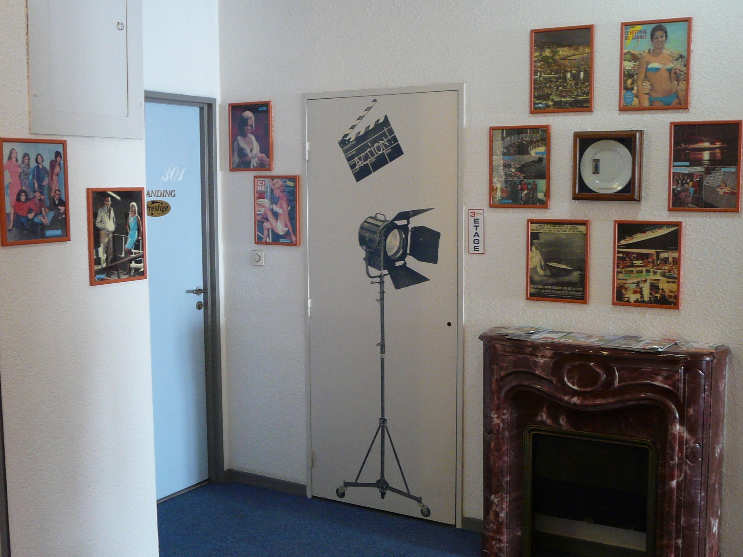 Un couloir avec une porte, une claquette de cinéma et divers tableaux encadrés accrochés aux murs.
