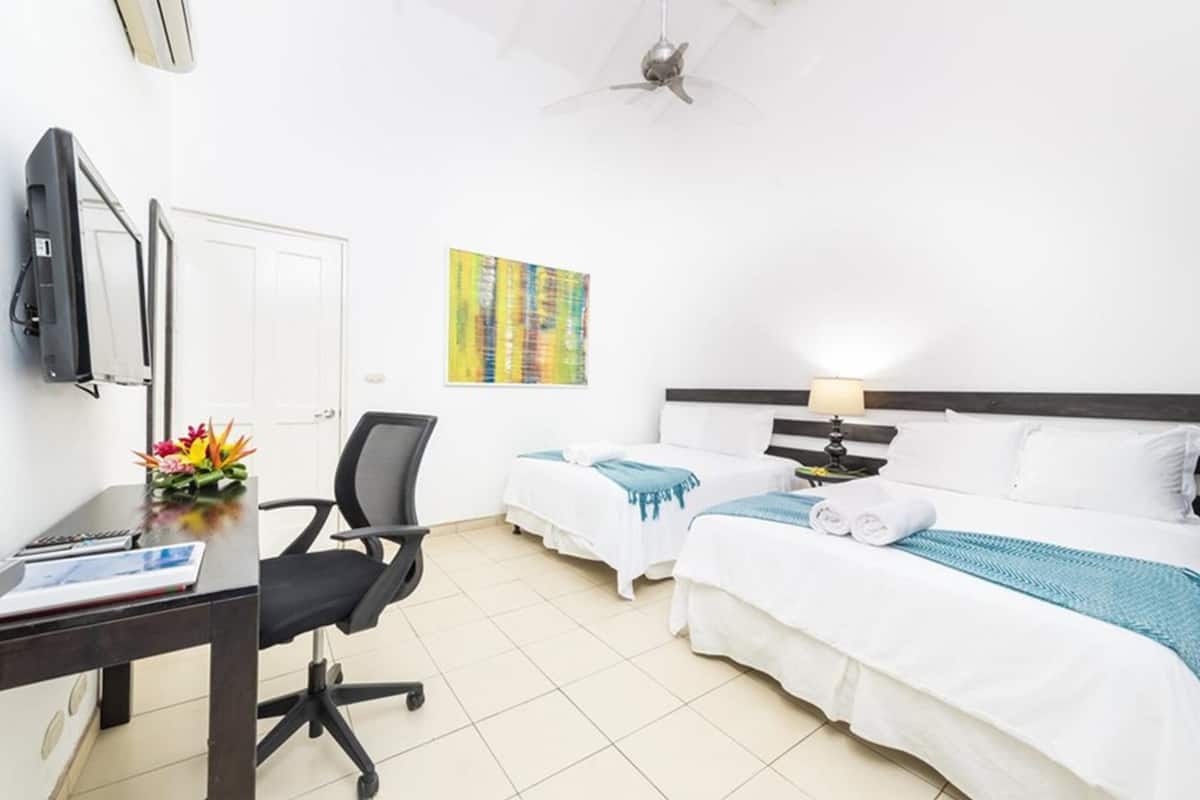 A hotel room with two beds, a desk with a chair, a TV, and a ceiling fan.
