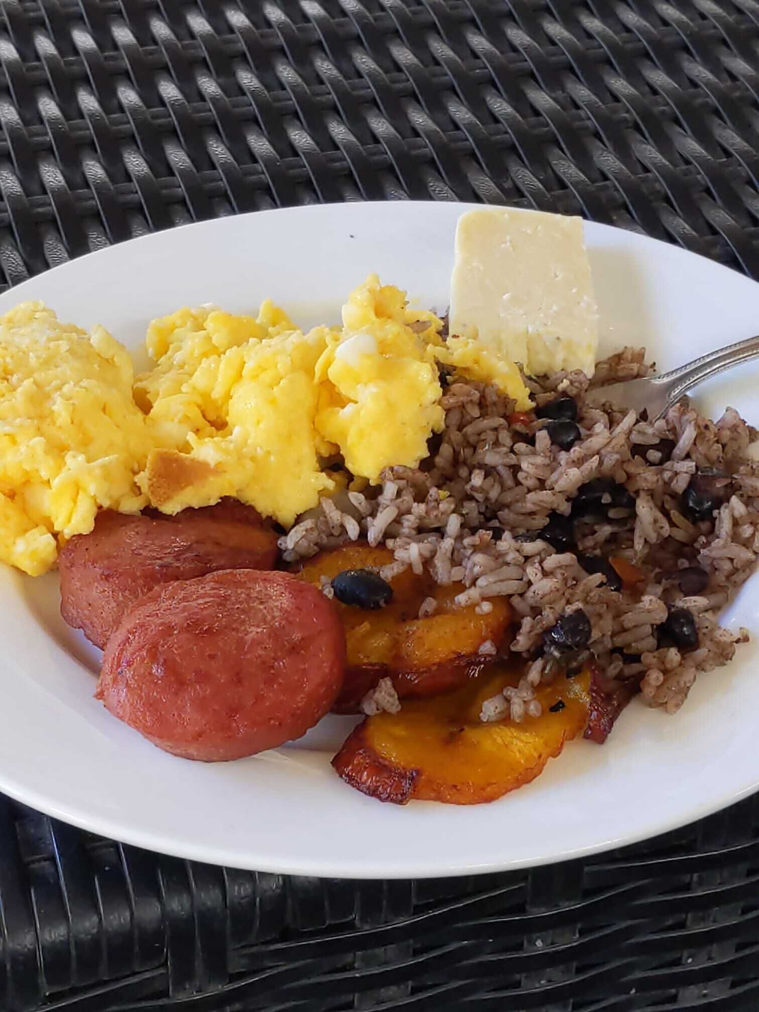 A plate with scrambled eggs, black beans, rice, and slices of meat.